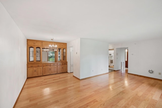 empty room featuring baseboards, light wood-style flooring, and a notable chandelier