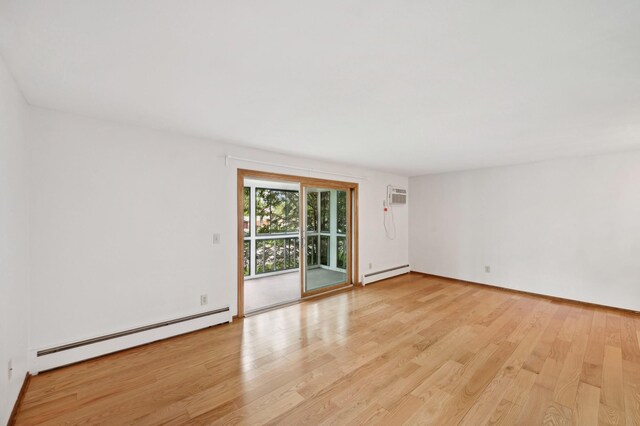 empty room with a baseboard radiator, light wood finished floors, and a wall unit AC