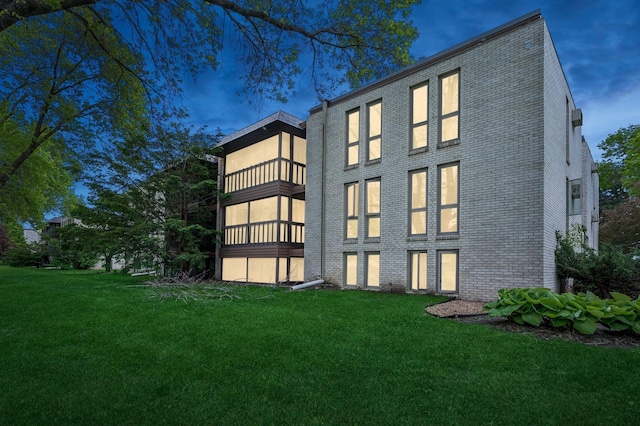 back of property featuring a yard, brick siding, and a balcony