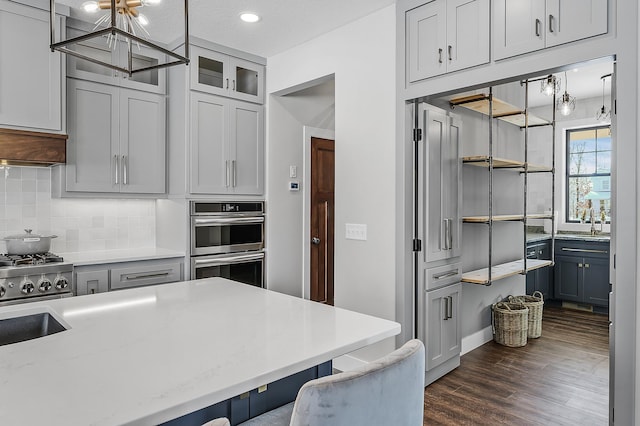 2451 180th Ln NE, Ham Lake, MN 55304 - kitchen featuring stainless steel double oven, dark wood-style flooring, a kitchen bar, tasteful backsplash, and a notable chandelier