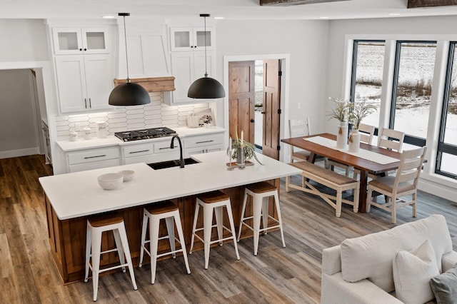 kitchen with decorative backsplash, wood finished floors, a center island with sink, gas cooktop, and a sink