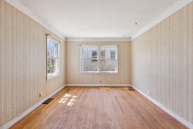 unfurnished room featuring baseboards, wallpapered walls, hardwood / wood-style flooring, and visible vents