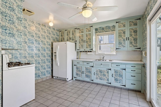kitchen with ceiling fan, wallpapered walls, light countertops, a sink, and white fridge with ice dispenser