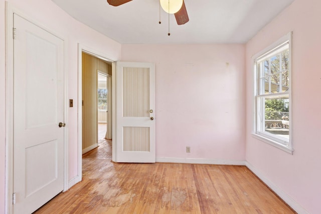 spare room with baseboards, light wood-style flooring, ceiling fan, and a wealth of natural light