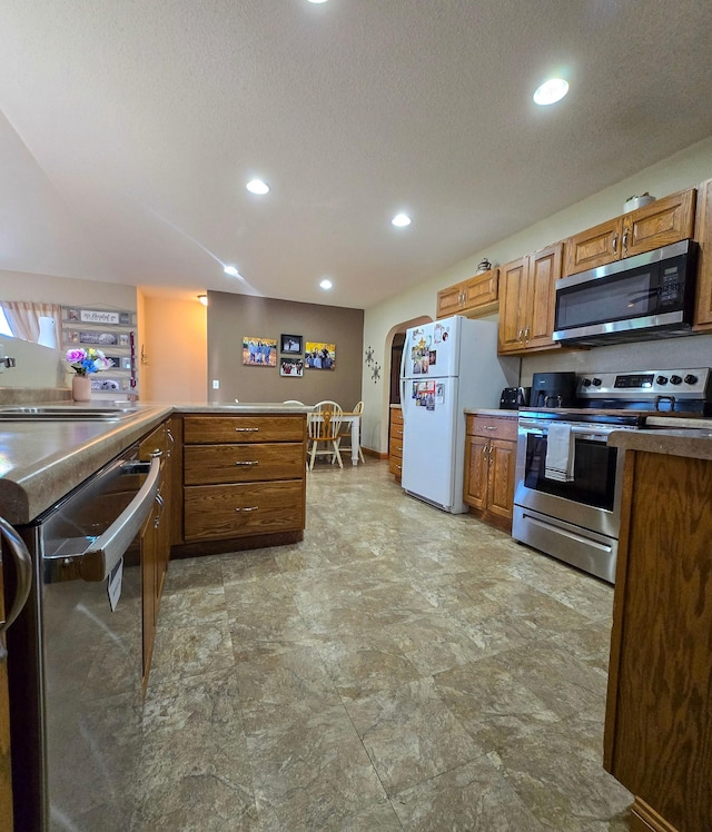 kitchen with brown cabinetry, a textured ceiling, arched walkways, stainless steel appliances, and recessed lighting