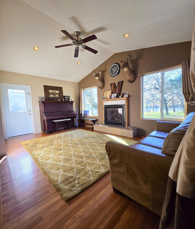 living area with a glass covered fireplace, a ceiling fan, recessed lighting, wood finished floors, and vaulted ceiling