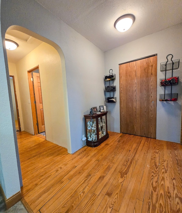 hallway with arched walkways, a textured ceiling, and wood finished floors
