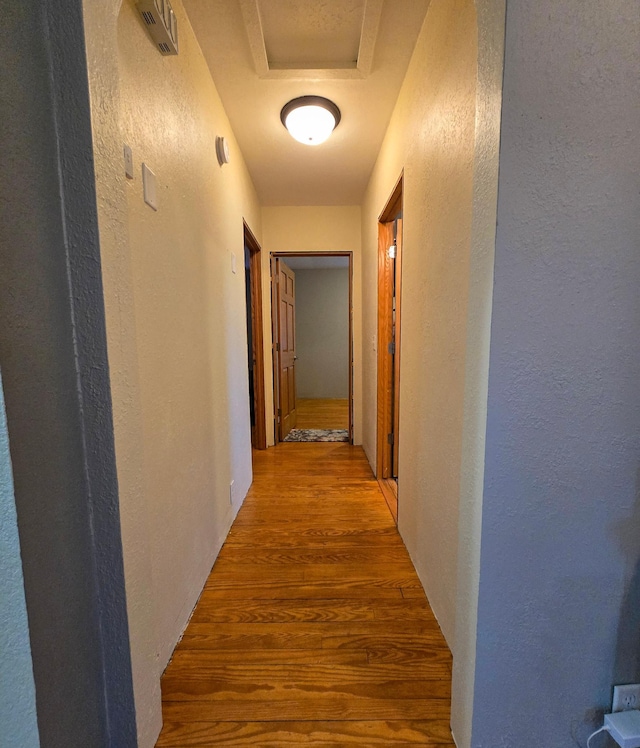 corridor with a textured wall, visible vents, and wood finished floors
