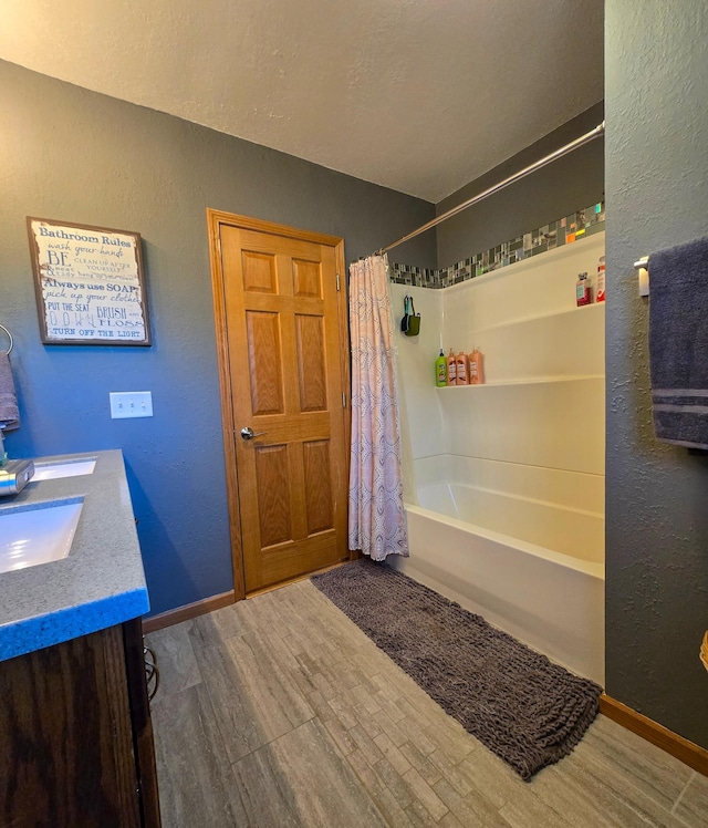 bathroom with shower / bath combo with shower curtain, vanity, a textured wall, wood finished floors, and baseboards