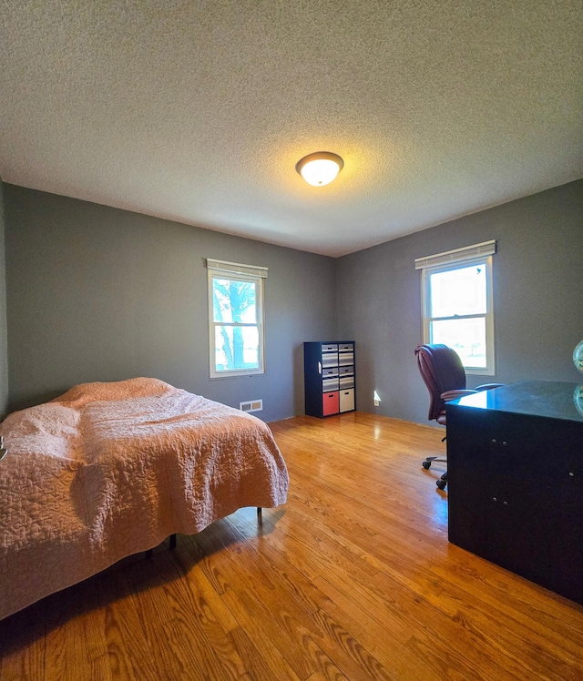 bedroom with visible vents, a textured ceiling, and wood finished floors