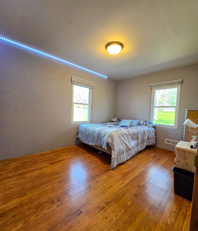bedroom with visible vents, wood-type flooring, and multiple windows
