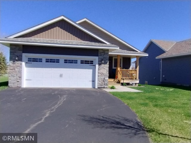 view of front of house featuring aphalt driveway, covered porch, a front yard, stone siding, and an attached garage