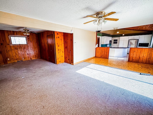 unfurnished living room with wooden walls, baseboards, ceiling fan, and carpet