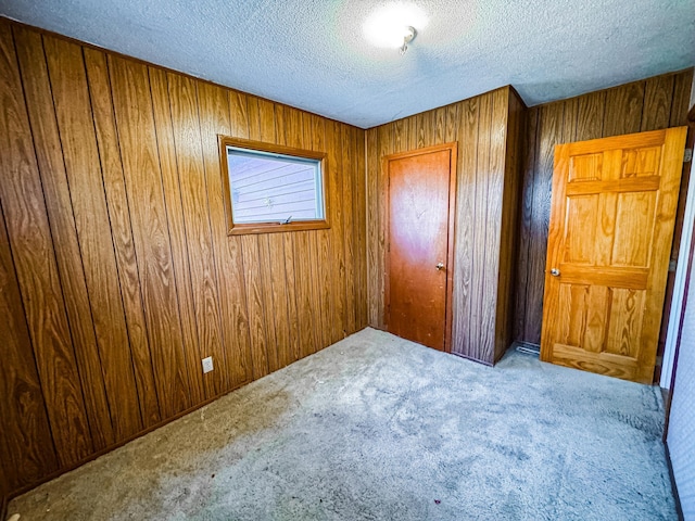 unfurnished bedroom with a closet, a textured ceiling, carpet, and wooden walls