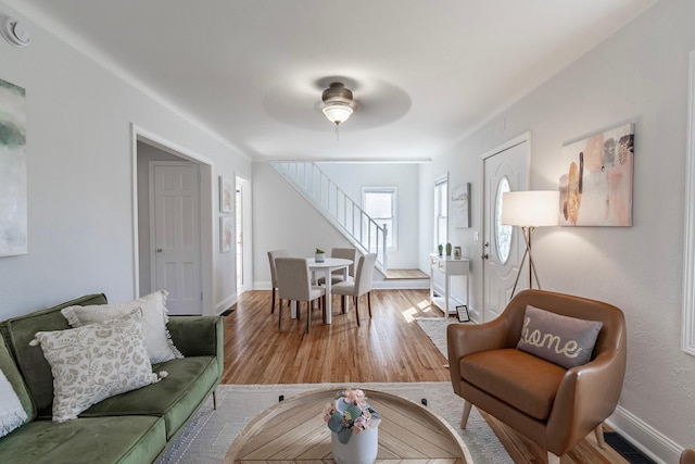 living room featuring a ceiling fan, visible vents, wood finished floors, stairway, and baseboards