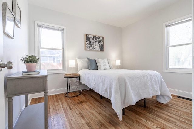bedroom featuring baseboards, visible vents, multiple windows, and light wood-type flooring