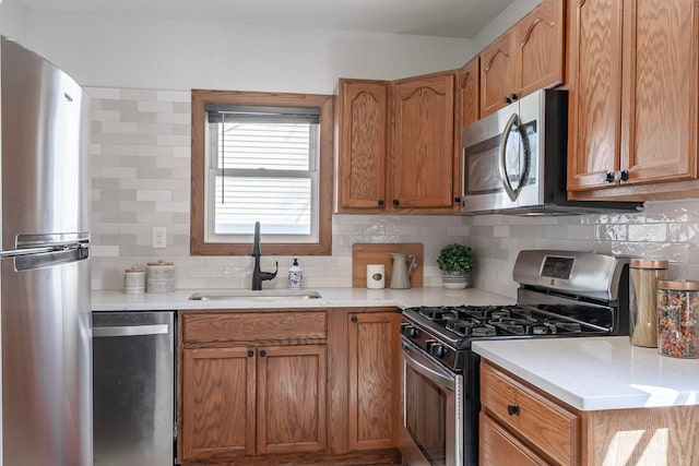kitchen with brown cabinetry, decorative backsplash, light countertops, a sink, and appliances with stainless steel finishes