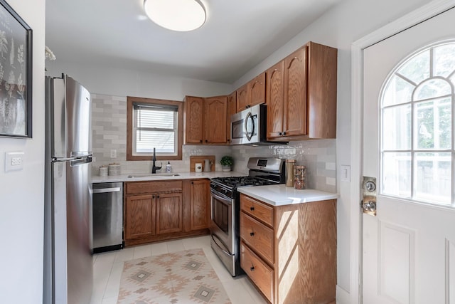 kitchen featuring brown cabinetry, tasteful backsplash, a sink, light countertops, and stainless steel appliances