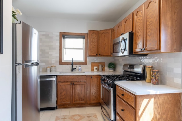 kitchen with light countertops, appliances with stainless steel finishes, brown cabinetry, and a sink