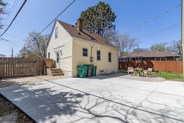 back of house with fence, a patio, a chimney, and a shingled roof