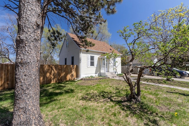view of side of property with fence, a lawn, and roof with shingles