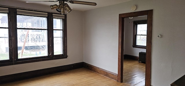 unfurnished room featuring light wood-style floors, baseboards, ceiling fan, and radiator heating unit