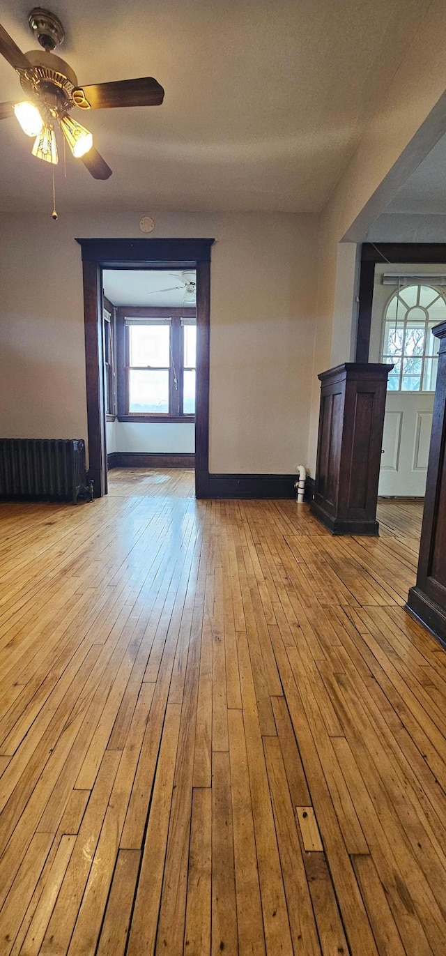 spare room featuring wood-type flooring, a ceiling fan, a wealth of natural light, and radiator heating unit