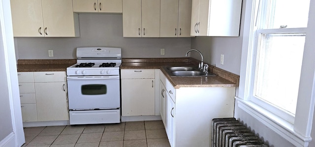 kitchen with dark countertops, gas range gas stove, radiator heating unit, a sink, and light tile patterned floors