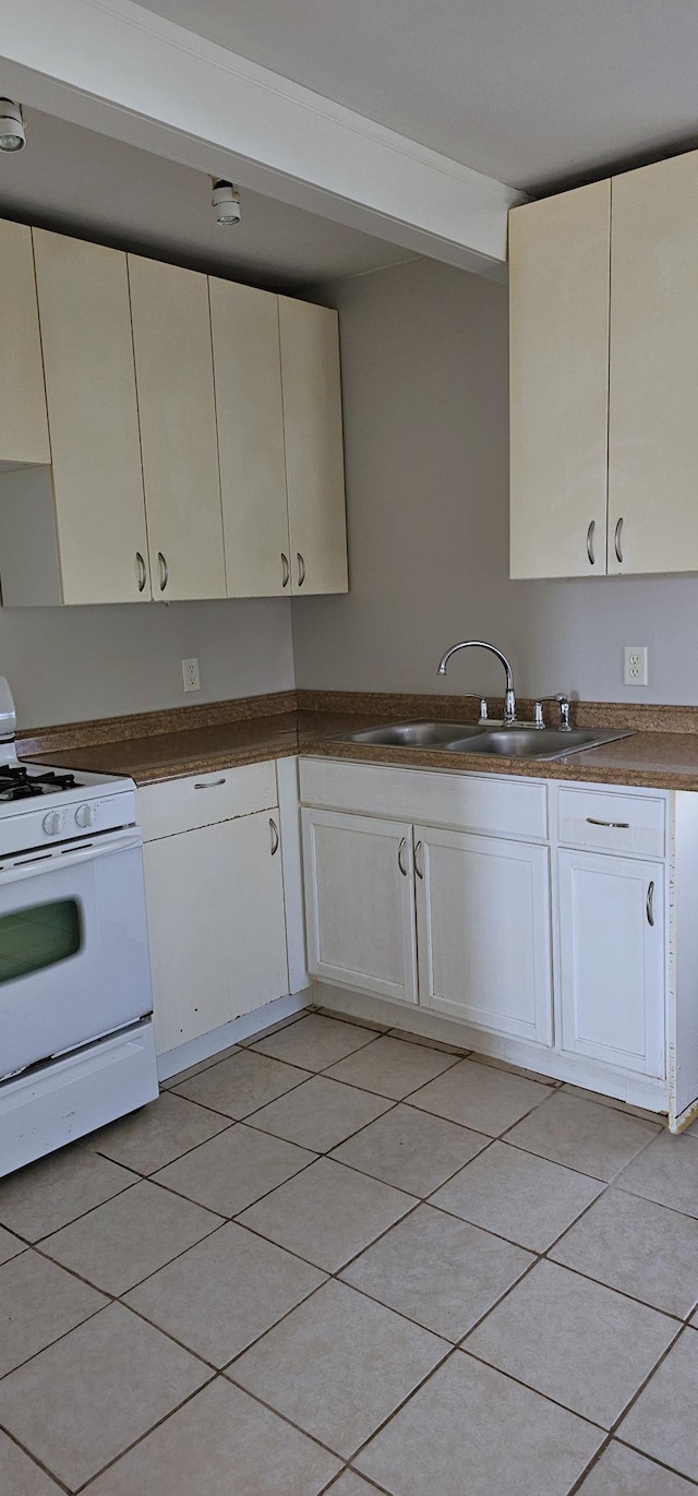 kitchen with a sink, white range with gas stovetop, cream cabinetry, and dark countertops