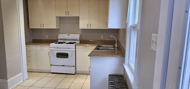kitchen featuring light tile patterned flooring, white gas range oven, a sink, white cabinetry, and baseboards