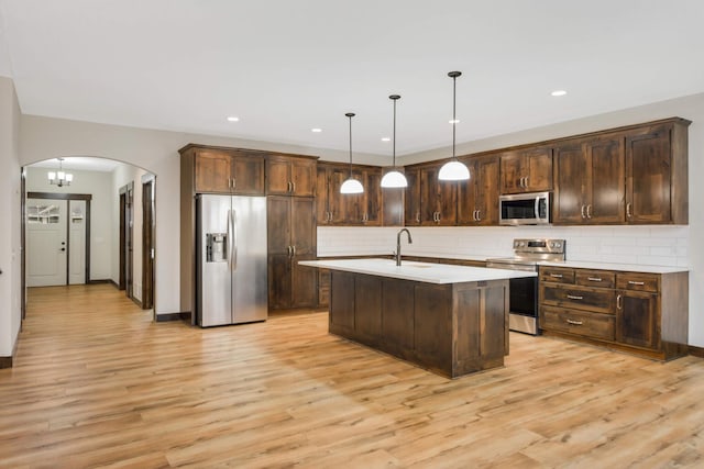 12891 Xylite St NE, Blaine, MN 55449 - kitchen with dark brown cabinetry, light countertops, arched walkways, light wood-style flooring, and appliances with stainless steel finishes