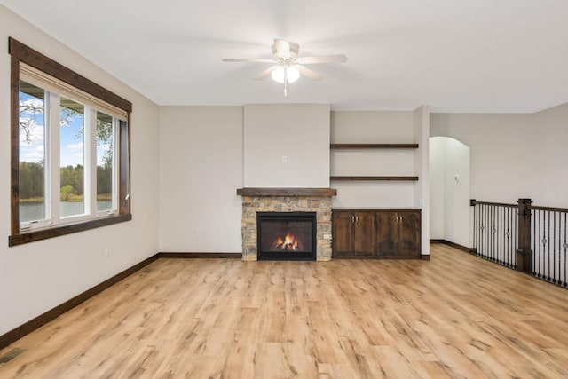 12891 Xylite St NE, Blaine, MN 55449 - unfurnished living room with visible vents, baseboards, a stone fireplace, a ceiling fan, and light wood-style flooring