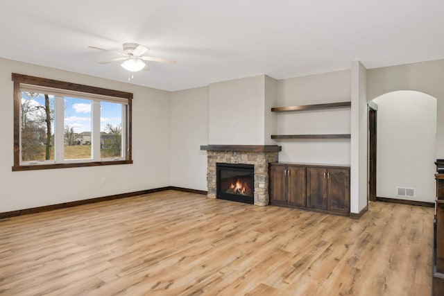12891 Xylite St NE, Blaine, MN 55449 - unfurnished living room with light wood finished floors, arched walkways, a stone fireplace, a ceiling fan, and visible vents