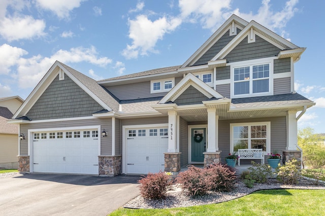 craftsman-style home featuring stone siding, driveway, covered porch, and roof with shingles