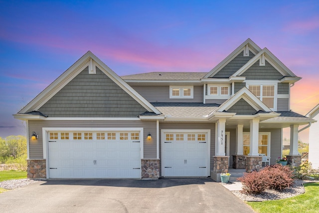 view of front of home with stone siding, driveway, a porch, a shingled roof, and a garage