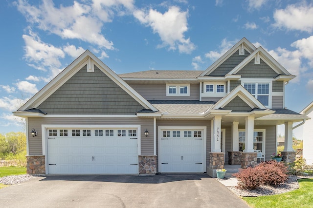 craftsman-style home with stone siding, driveway, a porch, roof with shingles, and a garage