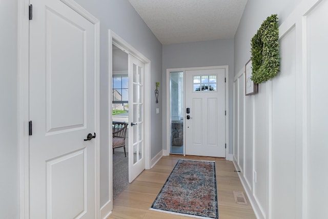 entryway with light wood-style floors, baseboards, and a textured ceiling