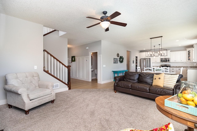 living room with light carpet, ceiling fan, stairs, a textured ceiling, and baseboards