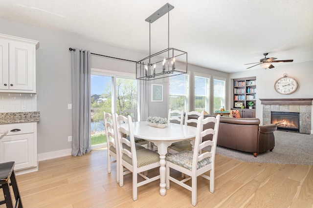dining space with light wood finished floors, a chandelier, a tile fireplace, ceiling fan, and baseboards