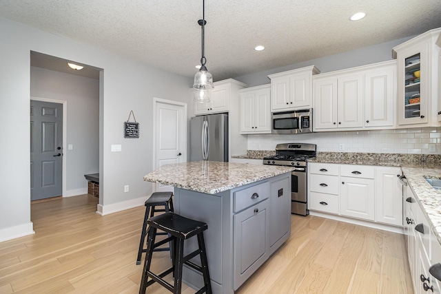 kitchen with stainless steel appliances, light wood-style floors, a center island, white cabinets, and decorative backsplash