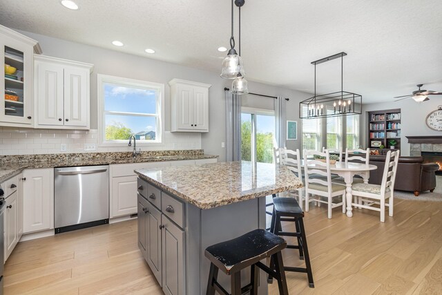 kitchen with dishwasher, a sink, open floor plan, white cabinetry, and a ceiling fan