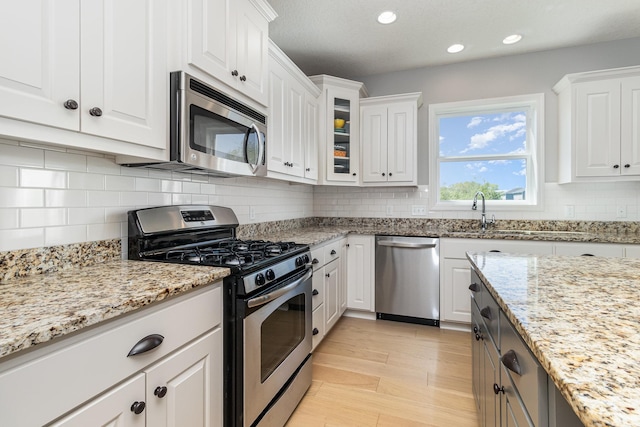 kitchen featuring appliances with stainless steel finishes, white cabinets, light stone countertops, glass insert cabinets, and recessed lighting