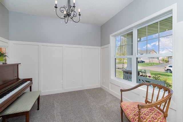 living area featuring a decorative wall, a chandelier, wainscoting, carpet flooring, and a textured ceiling