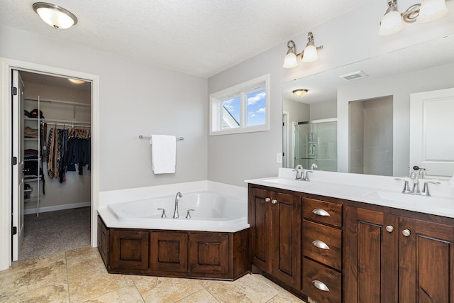 bathroom featuring double vanity, a shower stall, a bath, a walk in closet, and a textured ceiling