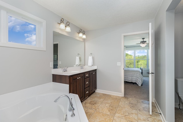 ensuite bathroom featuring double vanity, baseboards, a tub, ceiling fan, and a textured ceiling