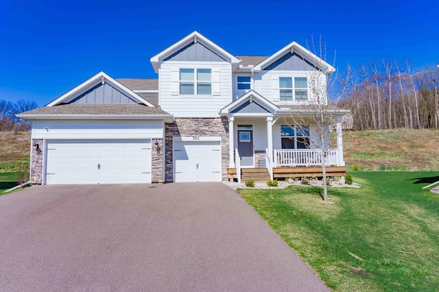 craftsman house featuring a front lawn, stone siding, board and batten siding, a porch, and driveway