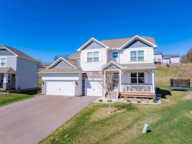 craftsman-style home with a trampoline, stone siding, aphalt driveway, board and batten siding, and a front yard