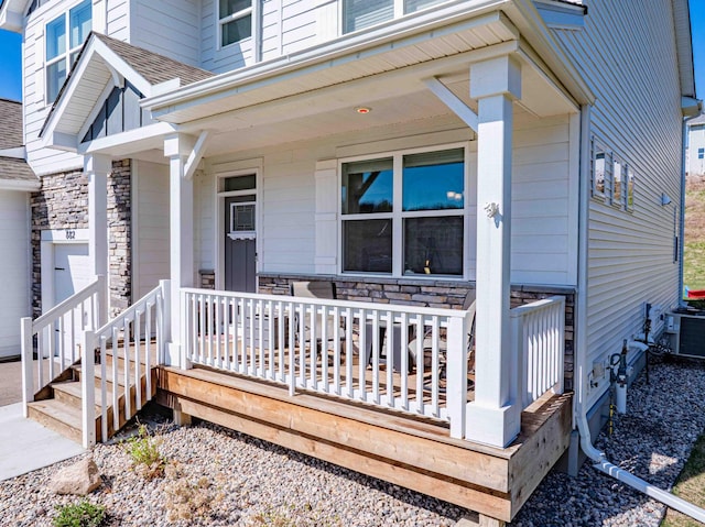 property entrance with a shingled roof, a porch, central AC, and stone siding