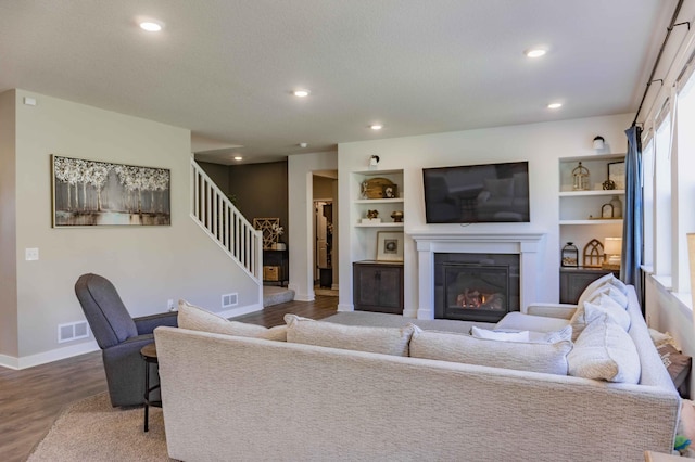 living room featuring a glass covered fireplace, baseboards, wood finished floors, visible vents, and stairway