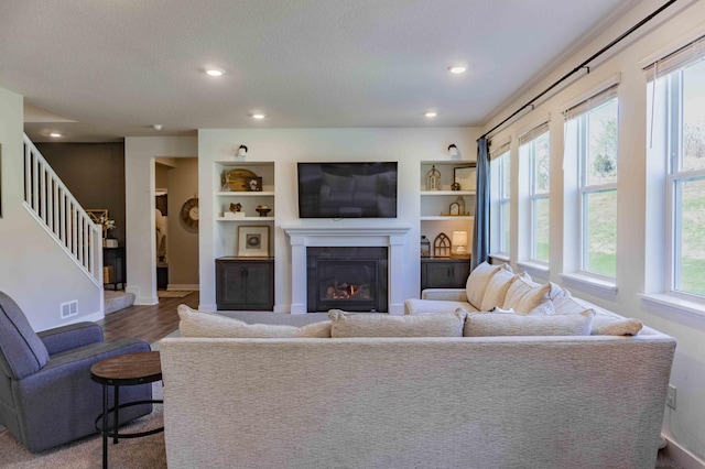 living area featuring visible vents, stairs, baseboards, a glass covered fireplace, and recessed lighting